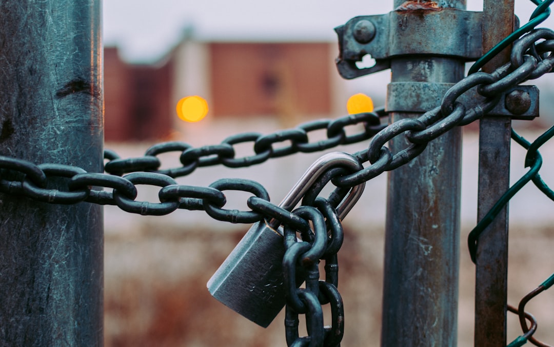 Un gros plan d’une chaîne métallique et d’un cadenas sécurisant un portail, symbolisant la sécurité robuste offerte par l’hébergement WordPress, avec des bâtiments flous et des lumières orange brillant en arrière-plan.